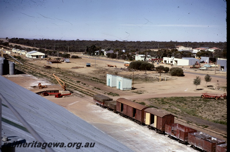 T05122
View of Kalannie, rake of vans and wagons, sidings, loading ramp, crane, trackside buildings, petrol station, town houses, Kalannie, KBR line, view from elevated position 
