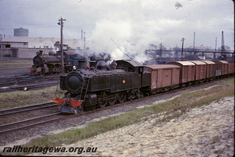 T05264
DM class 581, on goods train, another steam loco, rake of coal wagons, pedestrian overpass, crane, East Perth, ER line, front and side view

