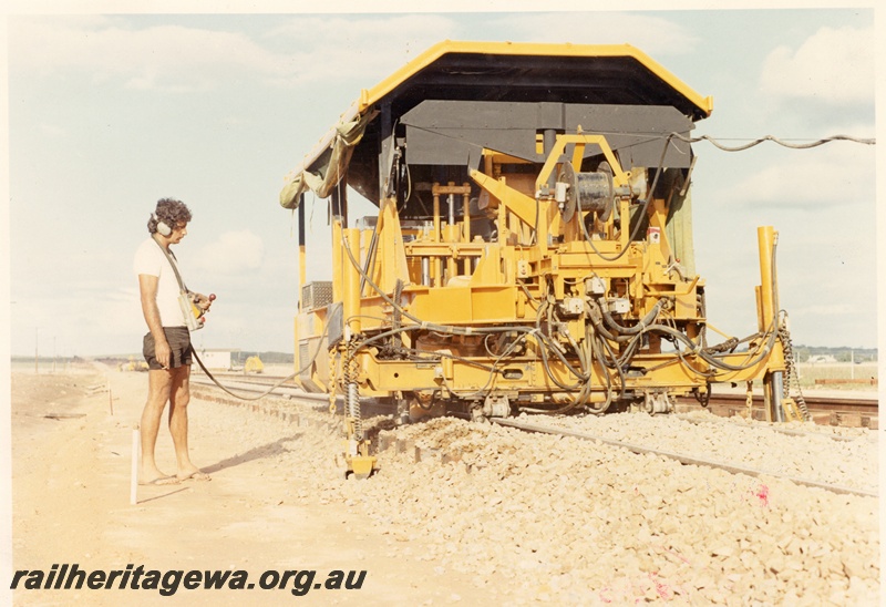 P01870
Track tamping machine with a worker wearing minimal safety clothing, side and end view
