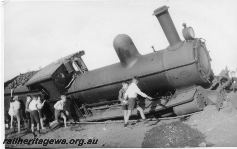 P01881
G class loco derailed and partially covered in dirt, side and front view, group pf boys inspecting the loco
