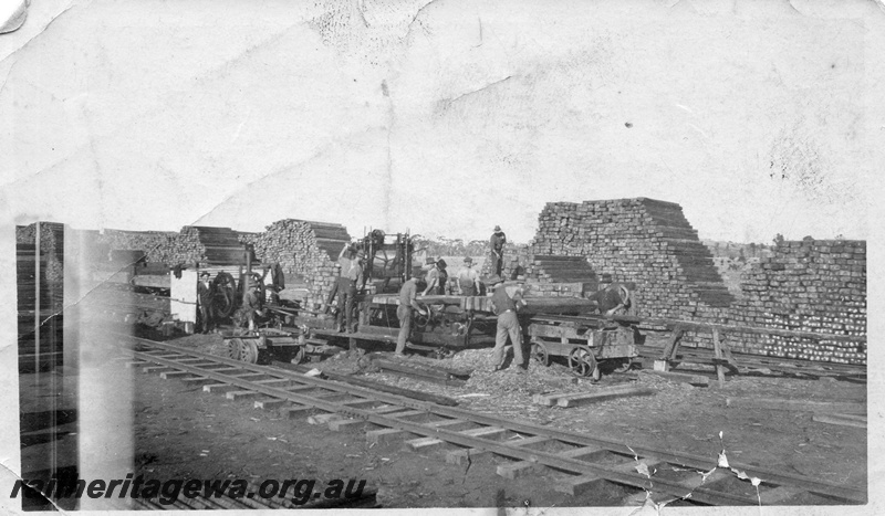 P01962
Track construction, Merredin, EGR line, stacks of sleepers, workers drilling holes in sleepers using a vertical drilling press.
