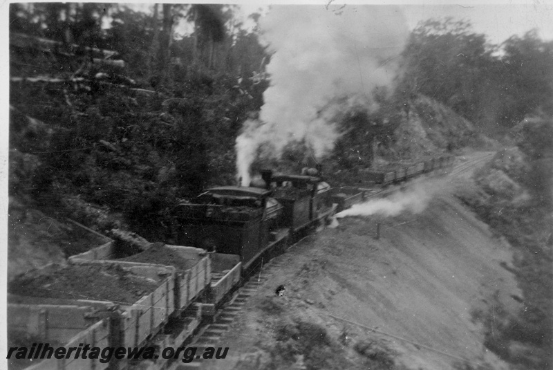 P02008
A pair of G class locos hauling a rake of side tipping wagons on the construction of the Denmark to Nornalup railway, D line, elevated view for the rear of the train looking towards the locos, c1928/29
