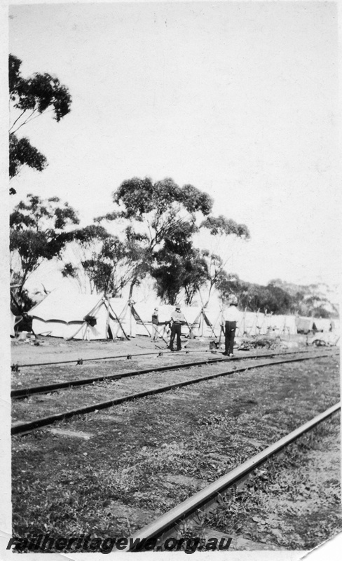 P02064
Construction workers standing in front of a row of tents beside the tracks
