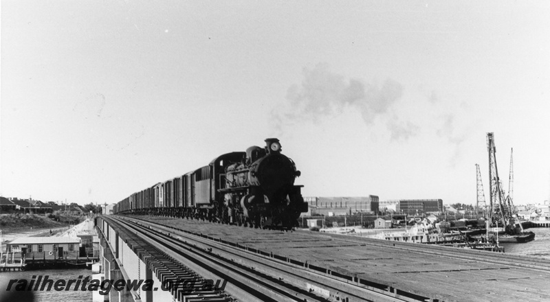 P02535
PMR class 724 steam locomotive, side and front view, crossing the Fremantle bridge, wool stores and harbour in the background, ER line. circa late 1960s.
