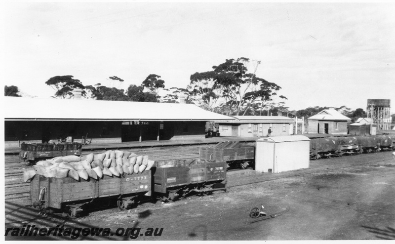 P02813
Station buildings including the refreshment room, 25,000 cast iron water tank on a water tower, GC class 7773 high sided open wagon laded with bagged wheat, GC class 7598 high sided open wagon, and other loaded wagons in the yard, Wagin, GSR line.
