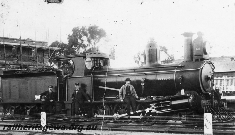 P02823
G class 68 2-6-0 steam locomotive, side view, driver or fireman on the footplate, uniformed station officials leaning against the loco, fireman or driver holding an oilcan sitting on the running board, signal wires, platform in the background. 

