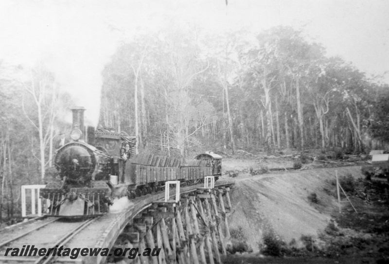 P02953
SSM G class 57 steam locomotive, hauling a rake of loaded open wagons and brakevan crossing a trestle bridge, crew on the footplate, vertical steam boiler at a log landing, horse team, log bridge, whim, in the bush at Pemberton.
