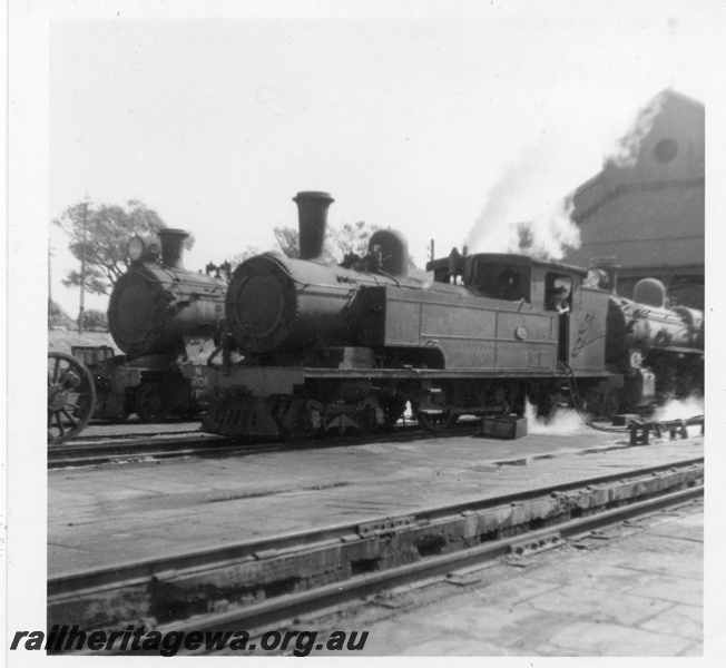 P03434
N class 201 steam locomotive, in steam at loco shed, front and side view, ash pit in foreground, East Perth, ER line.
