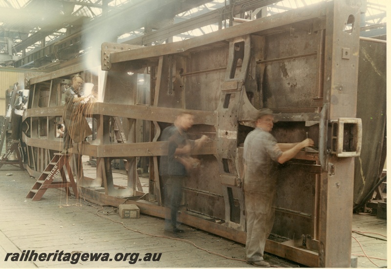 P03857
Construction underframe flat top wagon. View of workmen and underside of wagon.
