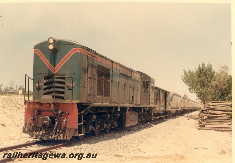 P03885
1 of 2, R class 1905 diesel locomotive on bauxite train, green with red and yellow stripes livery, running long hood first, front and side view, XC class bauxite hoppers.

