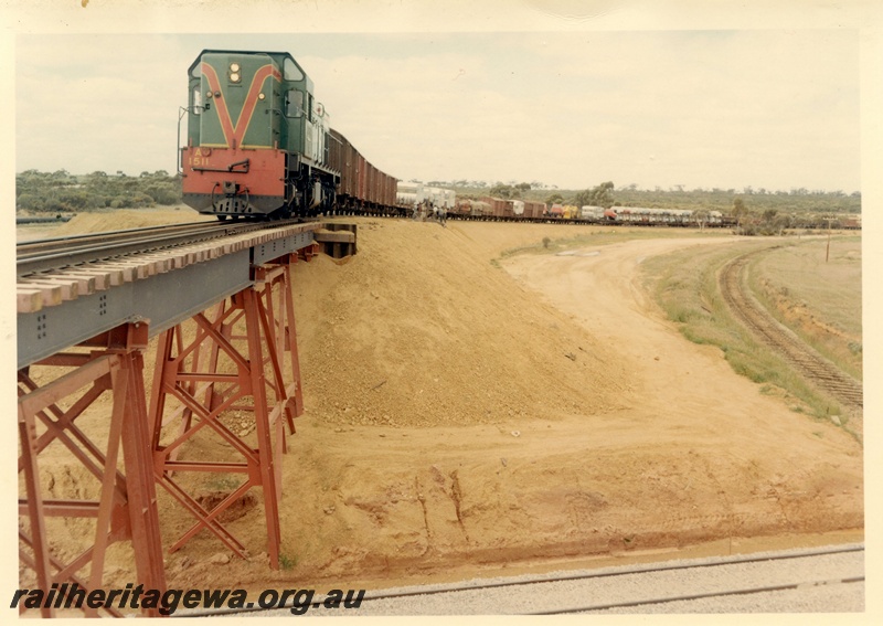 P03994
A class 1511 diesel locomotive in green with red and yellow stripe livery, on goods train, crossing standard gauge flyover with original EGR line to the side, standard gauge line in foreground, standard gauge construction project.
