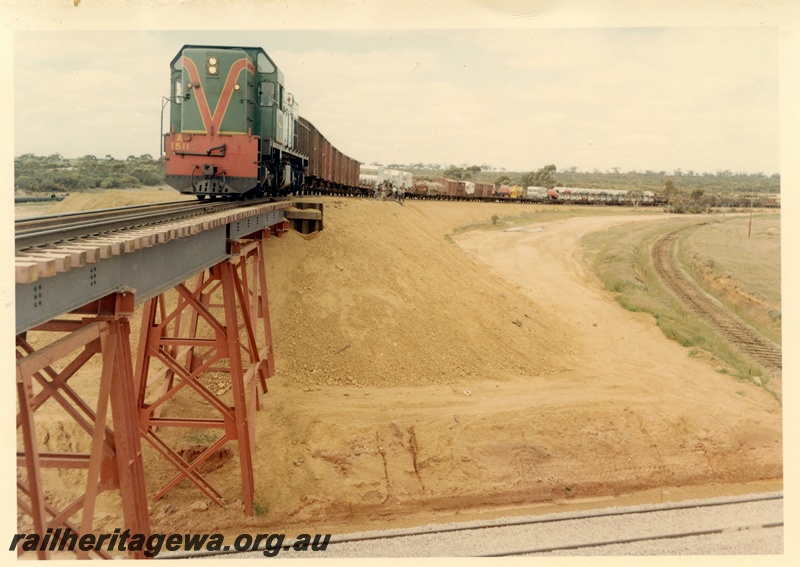 P03994
A class 1511 diesel locomotive in green with red and yellow stripe livery, on goods train, crossing standard gauge flyover with original EGR line to the side, standard gauge line in foreground, standard gauge construction project.
