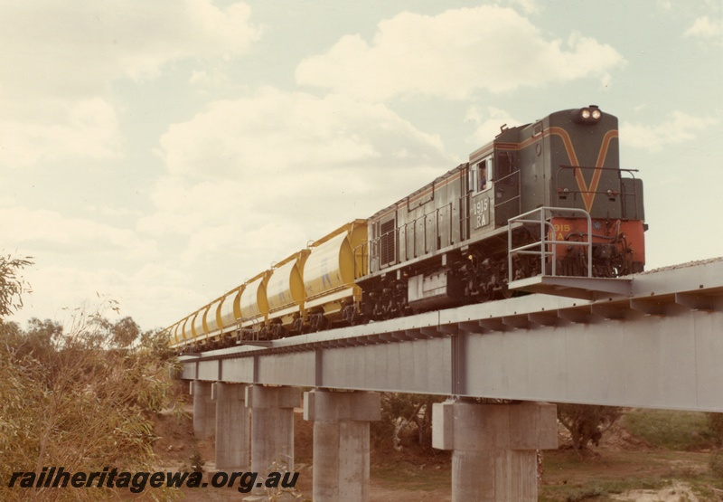 P04027
1 of 2 images, RA class 1915, green with red and yellow stripe, hauling train of XE class mineral sand wagons, crossing steel and concrete bridge, Irwin River
