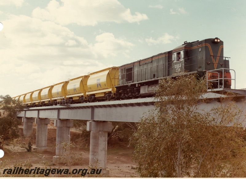 P04028
2 of 2 images, RA class 1915, green with red and yellow stripe, hauling train of XE class mineral sand wagons, crossing steel and concrete bridge, Irwin River
