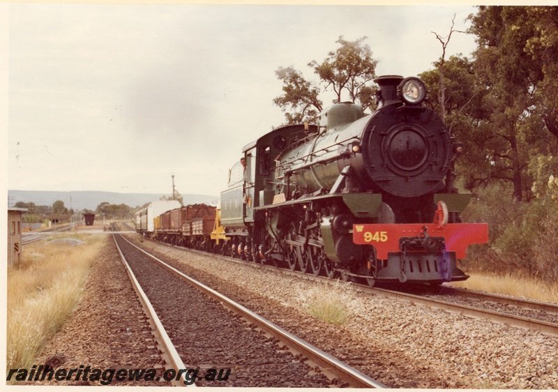 P04190
W class 945 steam locomotive, side and front view, on mixed goods train, passenger shelter and platform in the distance.
