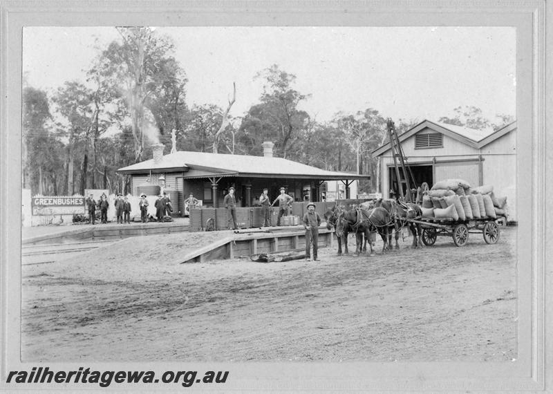 P10199
Station building, goods shed, loading platform yard crane, Greenbushes, PP line, group of men on the platform includes the station master, Mr F.S. Barnett on the far left. Horse drawn cart at the loading platform loaded with sacks
