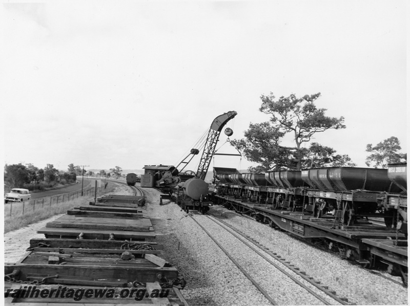 P10245
EX Commonwealth Railways (CR) four wheel ballast hoppers being loaded onto narrow gauge flat wagon by Cravens breakdown crane No 23, view along the line of wagons.
