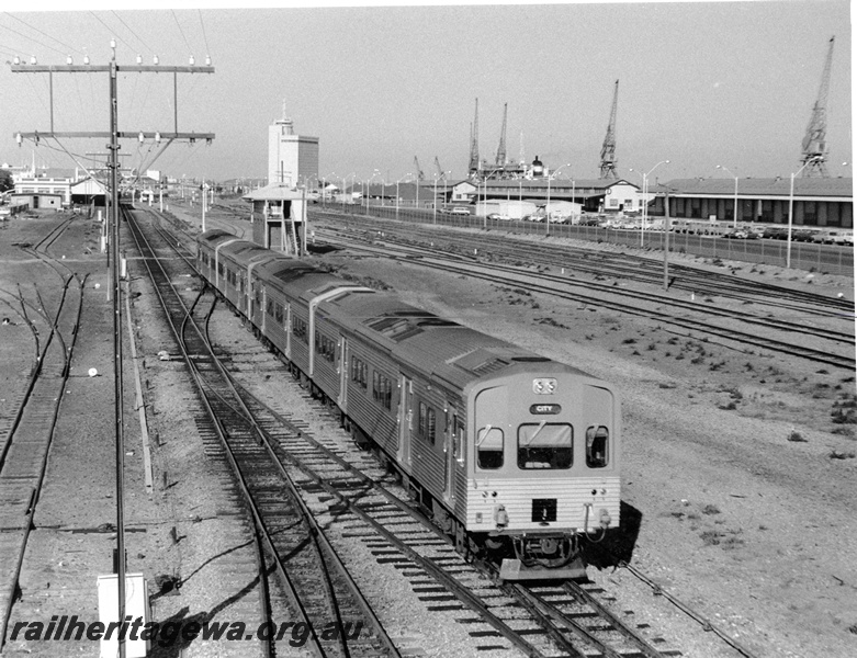 P10309
ADL class four car rail car set departing Fremantle for Perth, telegraph pole, signal box, Fremantle yard, station in the background, elevated view looking west.
