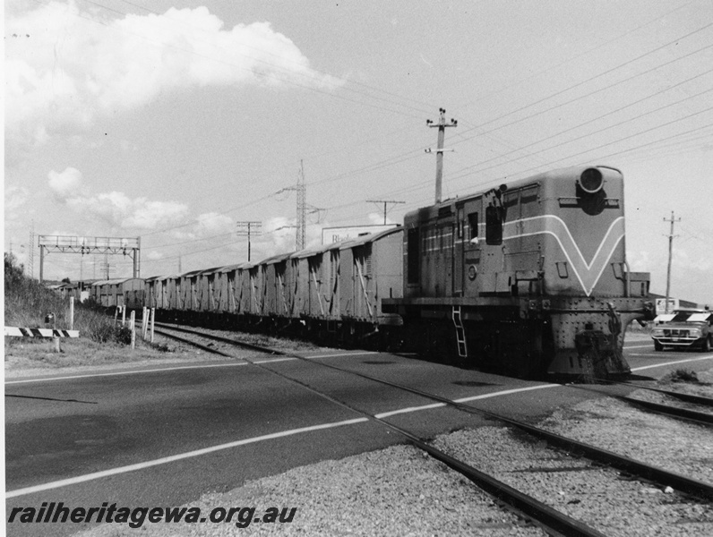 P10315
Y class loco in the Westrail orange livery hauling a train consisting of FD class vans over the Cockburn Road level crossing in Coogee, probably a wool train, signal gantry with searchlight signals in the background
