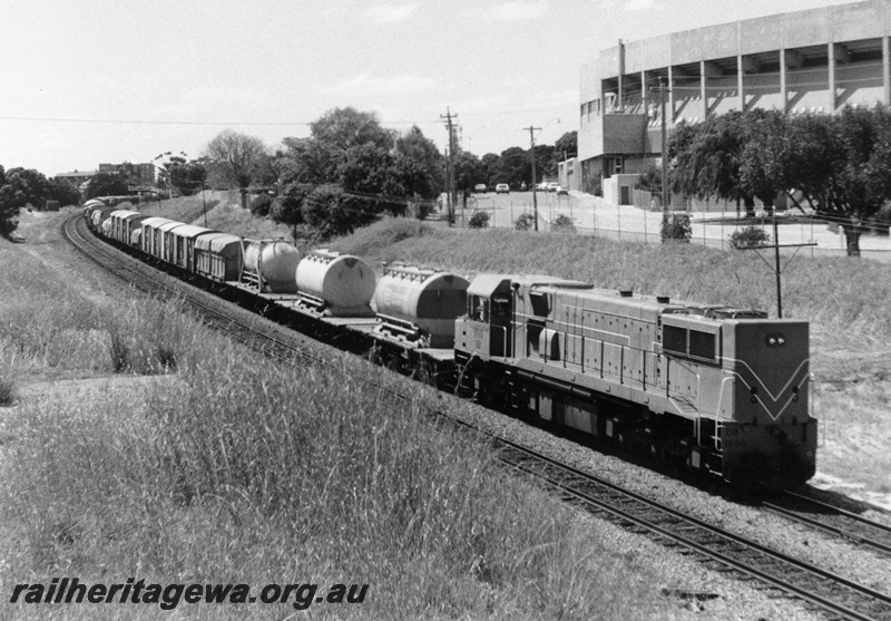 P10342
DB class diesel locomotive, long end leading, side and end view, Westrail orange livery, general freight, heading towards Fremantle, Subiaco football grandstands in the background.
