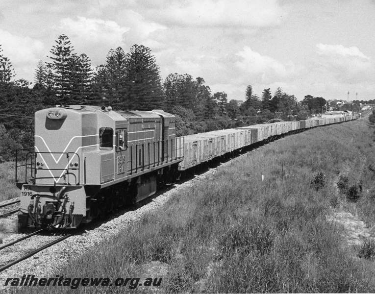 P10348
RA class 1916 Westrail Orange, short end and side view approaching Shenton Park heading towards Perth hauling rake of empty 4 wheel open wagons. Circa 1978
