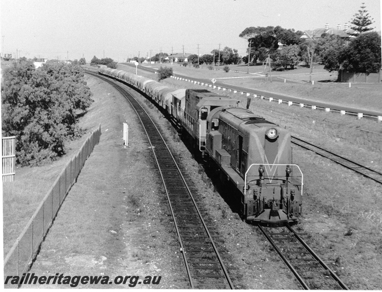 P10357
F class 46. Green with Red and Yellow Stripes hauling N class locomotive approaching Cottesloe heading for Forrestfield, long hood  leading,  hauling short train of 4 wheel tarpaulin covered wagons on down suburban line. Freight only Cottesloe Leighton line on right of photo.
