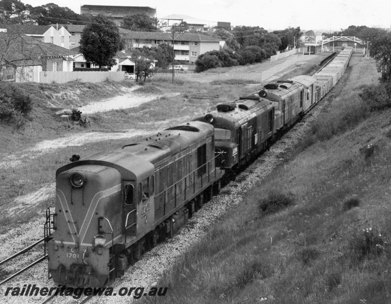 P10367
C class 1701 Green with Red and Yellow Stripes, leaving West Leederville, hauling two X class Diesels and train of empty four wheel open wagons. West Leederville Station and footbridge together with football stands at Subiaco Oval visible in background.
