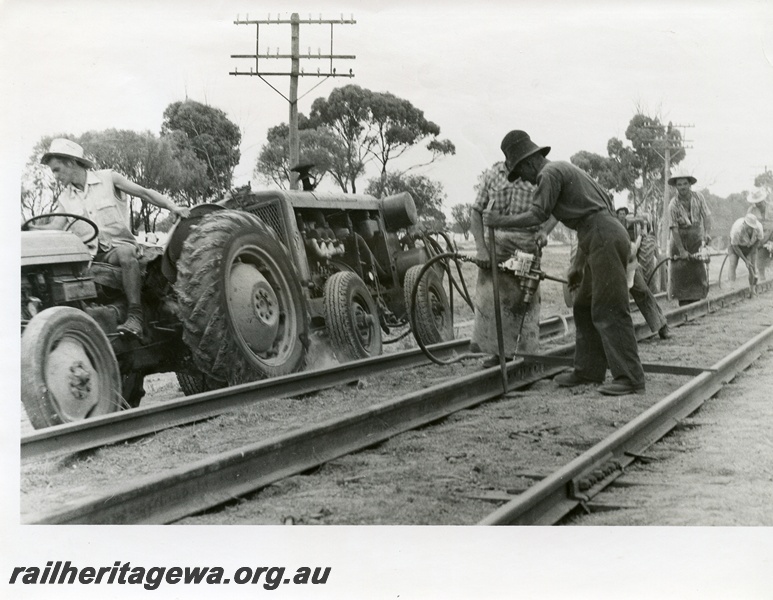 P10385
Track gang performing gauging work. Compressed air operated tools and tractor hauling 4 wheel compressor. Location Unknown.
