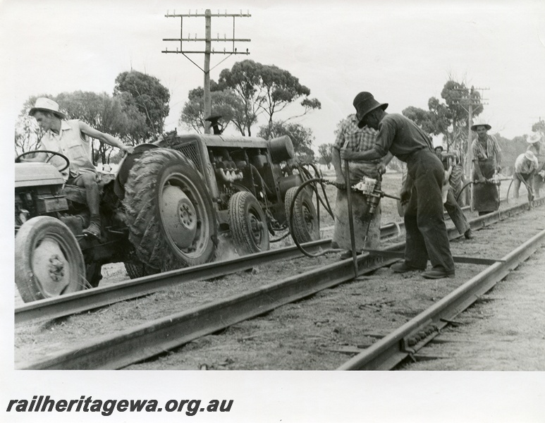 P10385
Track gang performing gauging work. Compressed air operated tools and tractor hauling 4 wheel compressor. Location Unknown.
