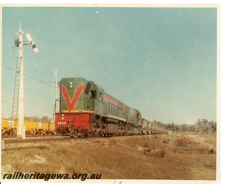 P10618
D class 1562 narrow gauge diesel locomotive, and a sibling locomotive, with a loaded bauxite train, of XB class wagons, arriving at Kwinana yard. To left of the train is part of a rake of stowed WO class ore wagons.
