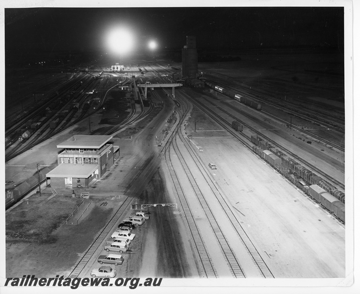 P10639
Night operations under spotlights at West Merredin dual gauge marshalling yard, yardmaster's office, carpark, gantry crane, grain transfer depot, locomotive depot, EGR line, view from elevated position
