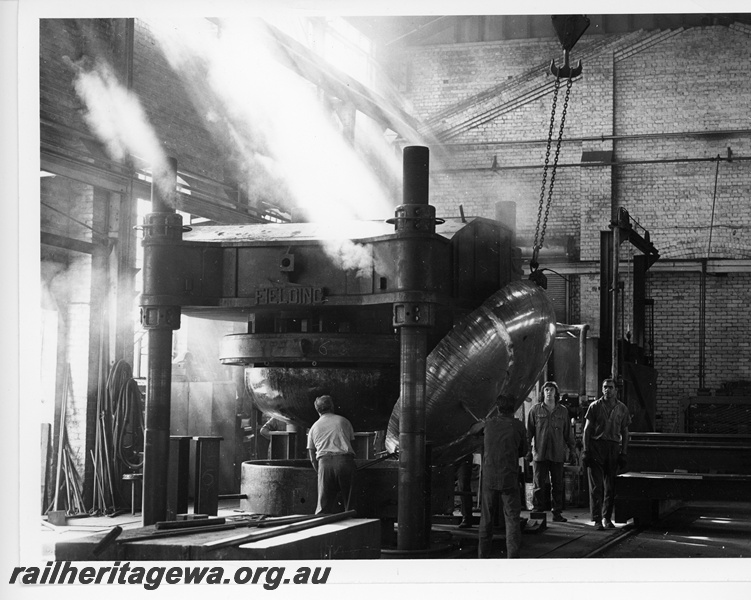 P10651
End of fuel tanker wagon being lifted after pressing, Fielding Press machine, workers, overhead hook and chain, sunbeams, Midland Workshops, floor level view
