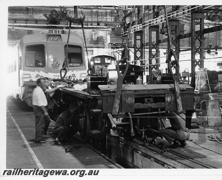 P10669
G class 233 4-6-0- steam locomotive striped down for restoration, frame suspended by straps from overhead hooks, inspection pit, workers, workshop paraphernalia, WCA class 