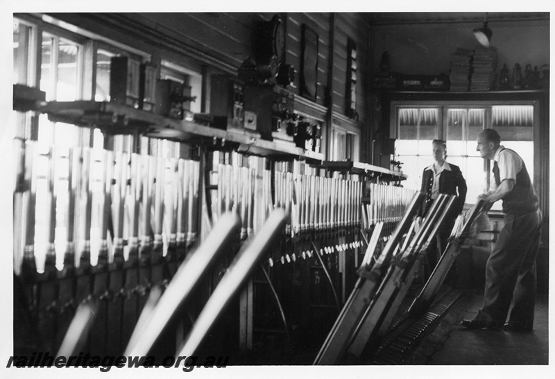 P10682
Interior view of a signal box with Signalman moving levers while the 'block boy' looks on.
