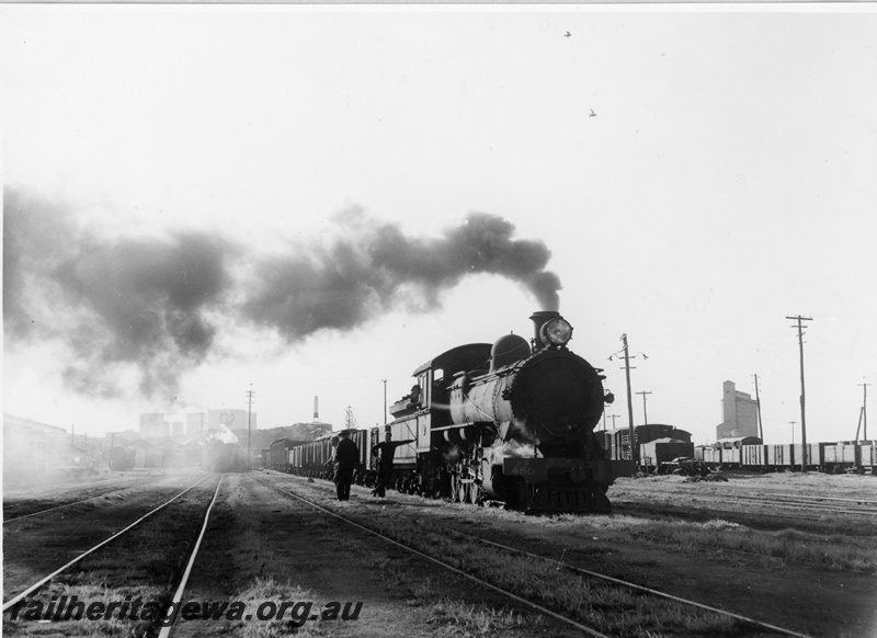 P10940
Fs class 450 steam locomotive shunting in the Bunbury goods yard. The loco crew and shunting crew are considering their next movements. Note the wheat silos in the background.
