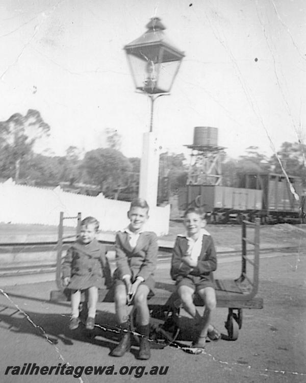 P12612
Platform trolley, station lamp, water tower, platform fencing, Clackline, ER line, three boys seating on the trolley
