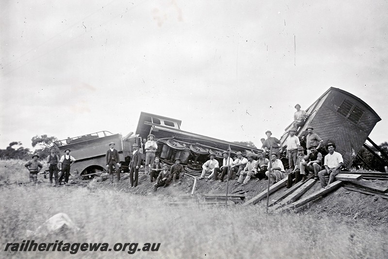 P12915
M class 2-6-0 loco, derailed surrounded by workers, side view of loco, end view of a van with diagonal planking on the end.
