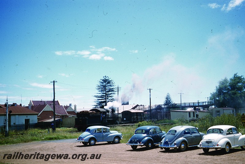 P13052
F class with wood fuel load in tender, Bunbury, SWR line, view of the rear of the tender. Three Morris Minor and a Volkswagen car in the carpark in the foreground.
