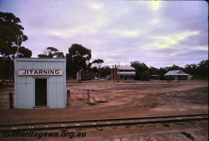 P13155
Out of Shed with nameboard, Jitarning, NKM line, trackside view, hotel in the far background.
