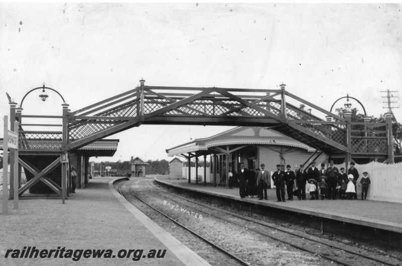 P13530
Footbridge, station buildings, Bayswater, signal box in the background, early photo, group of officials and other people on the platform, view along the tracks showing both platforms.
