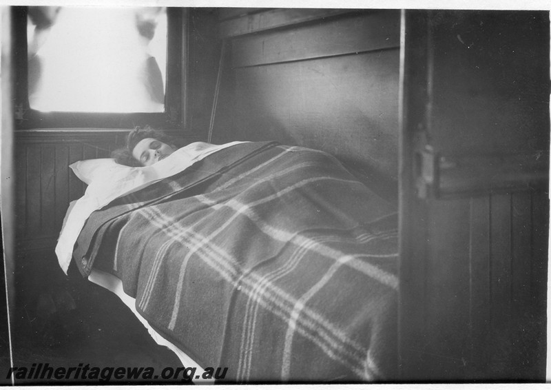 P13674
AQ class sleeping carriage, internal view of a compartment with the bed made up and passenger in the bed.
