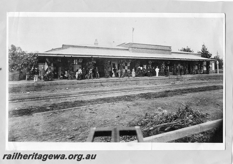 P13675
Station building, original Perth station, trackside view, large crowd on the platform which is decorated with flags and foliage on the occasion of the granting of self government to the colony of Western Australia on the 21st of October, 1890

