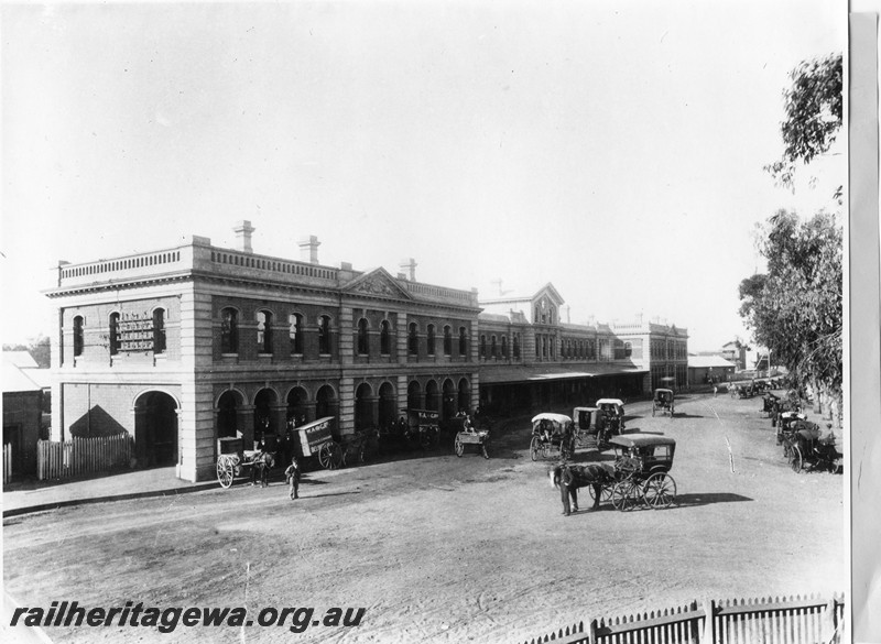 P13721
Station building, Perth, street side view with horse drawn vehicles in the forecourt.
