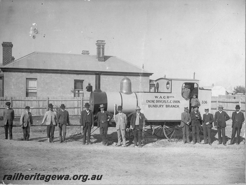 P13763
Mock up of a locomotive by the Bunbury Branch of the Engine drivers, F & C Union, Bunbury, side view. Men in suites lined up in front of the loco
