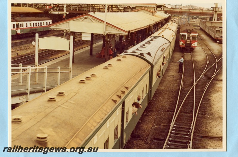 P14109
Perth station, with an A class diesel loco hauling a train of centre door AZ class passenger green and cream liveried carriages pulling in to number 8 platform. ADG railcar set in green, white and red livery and leading an ADA class railcar and a set of stainless steel bodied ADK/ADB railcar set, semaphore signals, ER line. 
