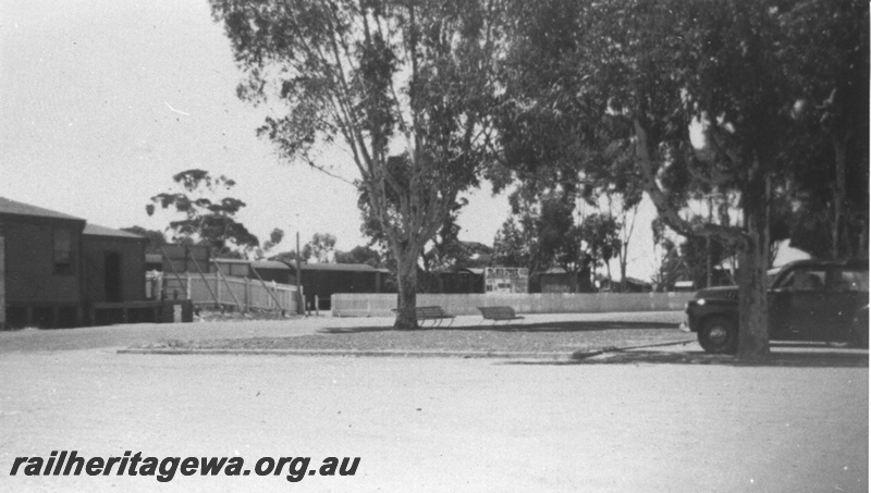 P14848
Partial view of rear of station building, advertising hoardings, picket fence, rolling stock, Kellerberrin, EGR line.
