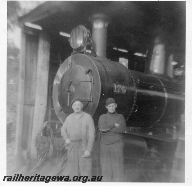 P14858
Bunnings YX class 176 steam locomotive, view of smoke box and front of boiler, in loco shed, two men posing for the photograph, Donnelly River Mill.
