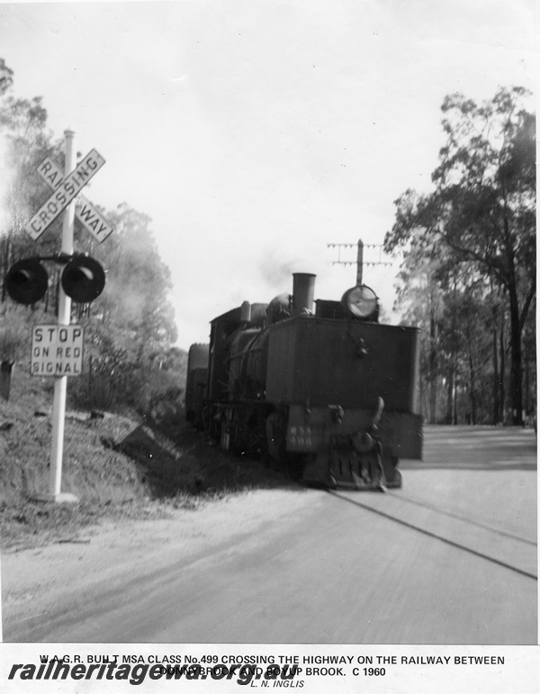 P14881
MSA class 499 Garratt articulated steam locomotive crossing the highway between Donnybrook and Boyup Brook, side and front view, railway crossing sign and lights, DK line, c1960.

