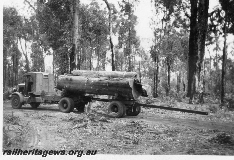 P14936
A semi trailer truck with a load of logs and a long rod extending from under the trailer
