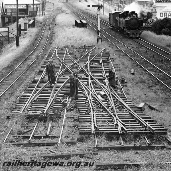 P14992
Pointwork, a scissors crossover incorporating a double slip laid out between the tracks ready to be pulled into position in the Perth Yard in West Perth, DD class 591 in the background hauling a goods train of two wagons and a brakevan, view along the yard.

